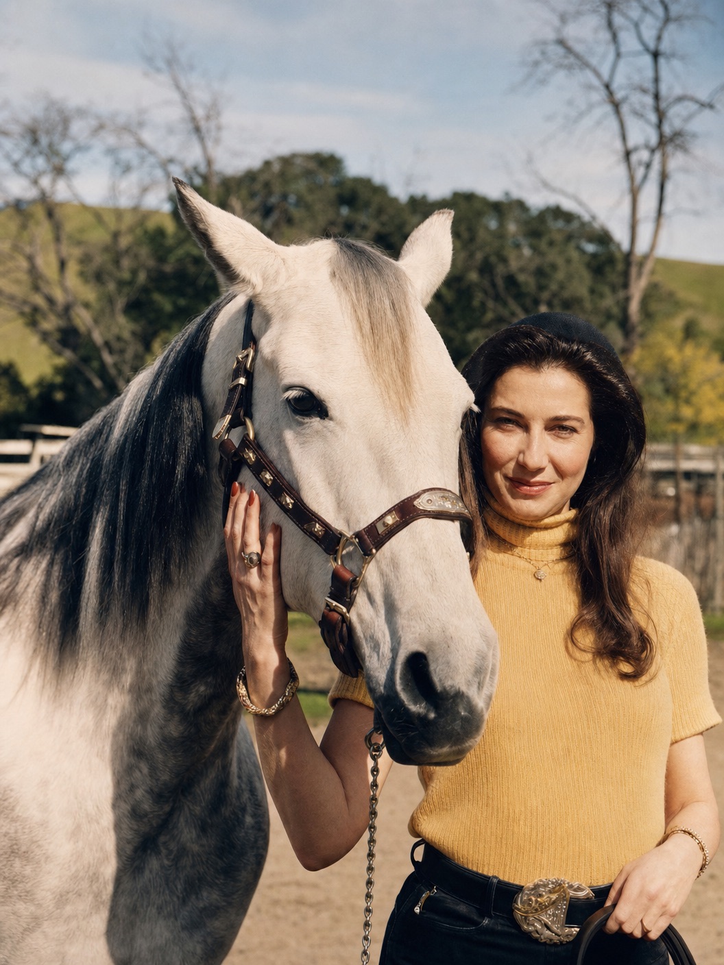 Carol Ellen Wall standing beside a grey horse in a sunlit paddock